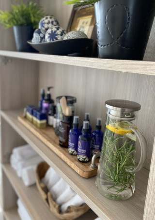 Shelves holding a water pitcher with herbs, massage oils and clean white towels.